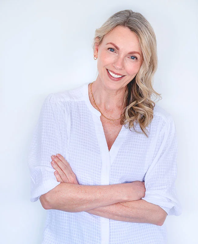 Middle aged woman post facelift, standing with arms folded and smiling