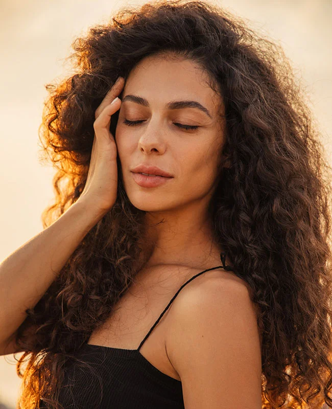 Curly haired woman gently touching the side of her face